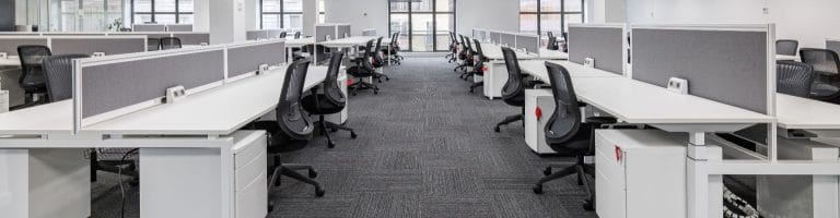 Inside of an office with numerous desks and office chairs.