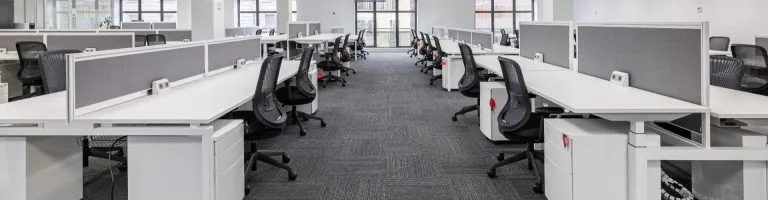 Inside of an office with numerous desks and office chairs.